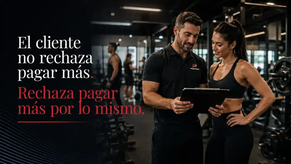 Imagen editorial dentro de un gimnasio moderno. Un coach revisa una tabla o clipboard junto a una socia, mostrando atención personalizada y acompañamiento. En el fondo se observan personas entrenando y equipo de gimnasio, mientras el diseño comunica que el valor percibido depende de la experiencia, no solo del precio.