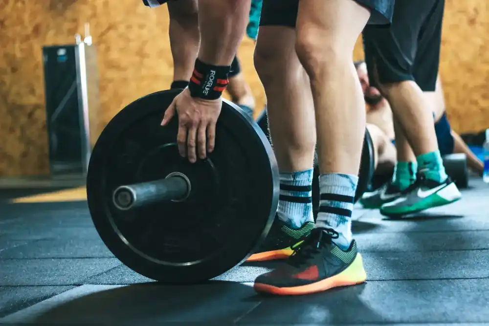 Personas entrenando con equipo de fuerza dentro de un gimnasio con alta actividad.